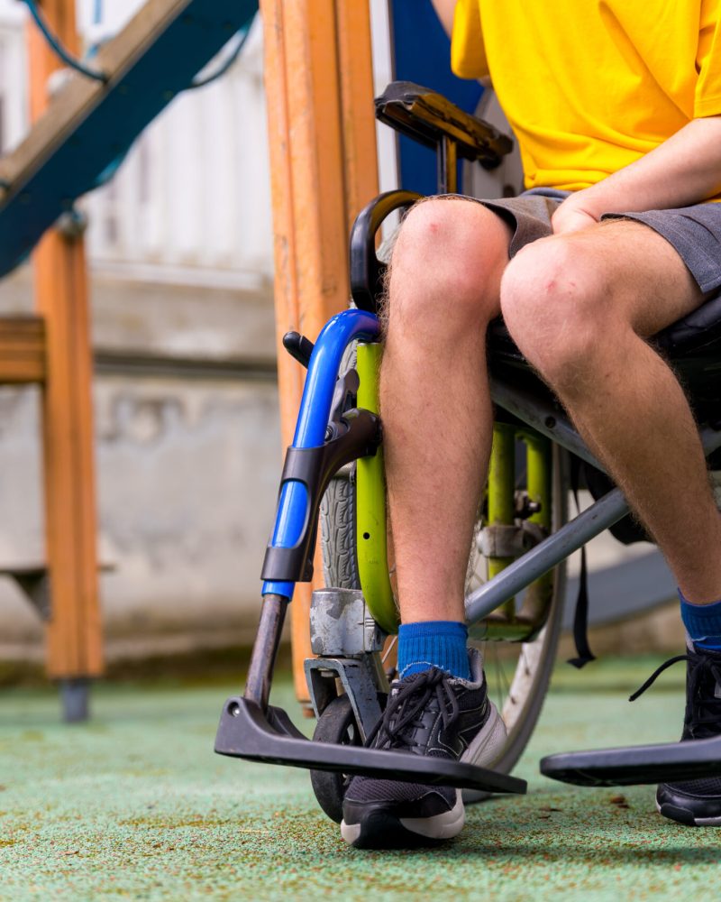 Detail of a disabled person in a wheelchair on the swings of a playground