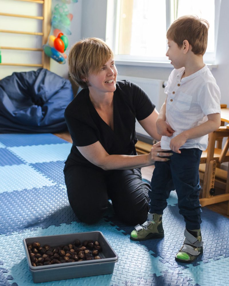 A therapist assists a young boy with cerebral palsy during his rehabilitation exercises in a vibrant therapy room.